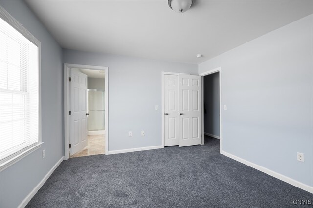 unfurnished bedroom with dark colored carpet, a closet, connected bathroom, and baseboards