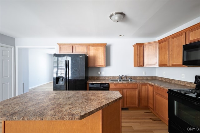 kitchen featuring light wood-style flooring, a kitchen island, a sink, black appliances, and dark countertops