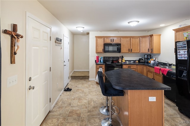 kitchen featuring baseboards, dark countertops, a kitchen breakfast bar, a center island, and black appliances