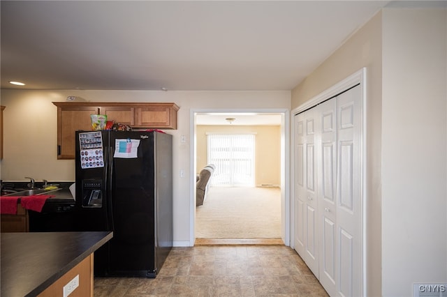 kitchen with dark countertops, stone finish floor, brown cabinets, black refrigerator with ice dispenser, and a sink