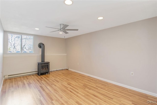 spare room featuring light wood finished floors, a baseboard radiator, recessed lighting, a wood stove, and baseboards