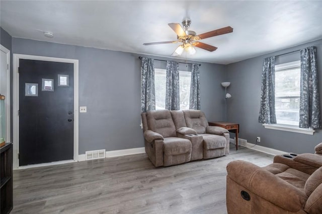 living area featuring a ceiling fan, visible vents, baseboards, and wood finished floors