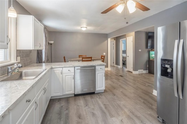 kitchen with a peninsula, a sink, light countertops, appliances with stainless steel finishes, and light wood finished floors