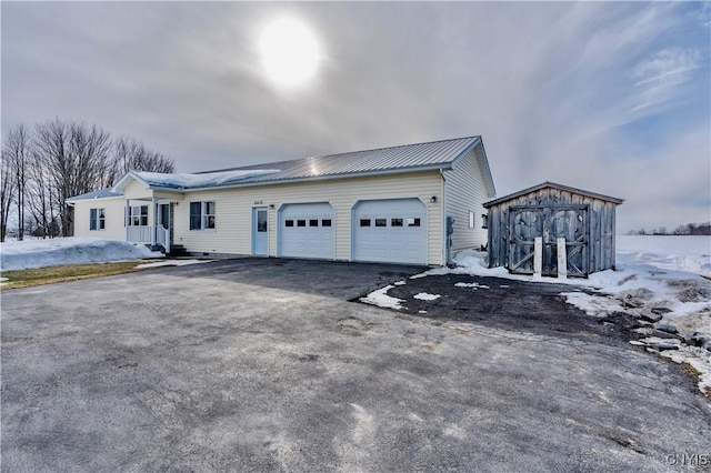 view of front facade featuring an outbuilding, metal roof, aphalt driveway, an attached garage, and a storage unit