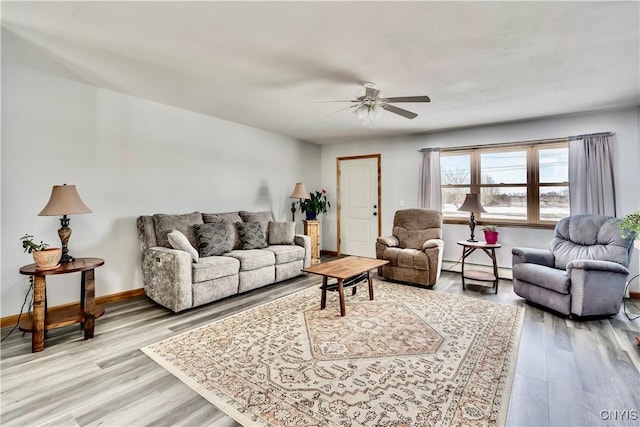 living area with a baseboard heating unit, ceiling fan, light wood finished floors, and baseboards