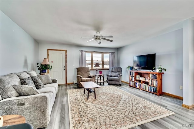 living area featuring a ceiling fan, a baseboard radiator, baseboards, and wood finished floors