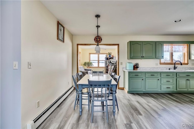 dining space featuring a healthy amount of sunlight, light wood-style floors, baseboards, and a baseboard heating unit