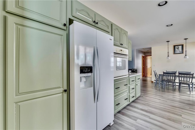 kitchen with white appliances, hanging light fixtures, light countertops, light wood-type flooring, and green cabinetry