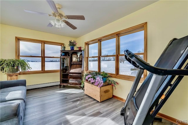 exercise room with a ceiling fan, baseboards, light wood-style flooring, and baseboard heating