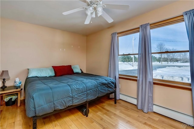 bedroom with light wood-style floors, ceiling fan, and baseboard heating