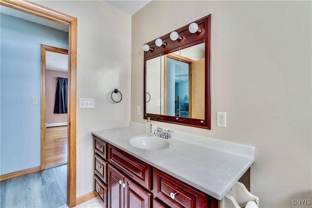 bathroom with a baseboard heating unit, wood finished floors, vanity, and baseboards