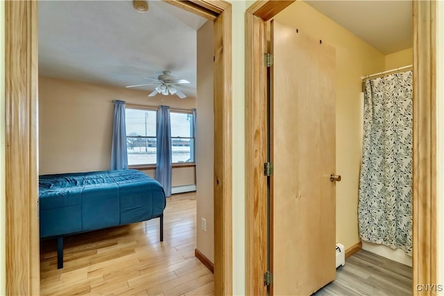 bedroom with a baseboard radiator, baseboards, and light wood finished floors