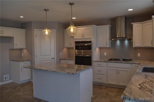 kitchen featuring double oven, wall chimney range hood, light stone counters, and white cabinetry