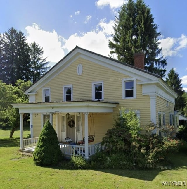 back of house featuring a chimney, a porch, and a lawn