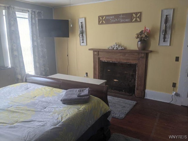 bedroom with crown molding, wood finished floors, a fireplace with flush hearth, and baseboards