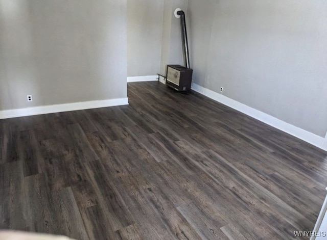 unfurnished living room featuring dark wood-type flooring, a wood stove, and baseboards