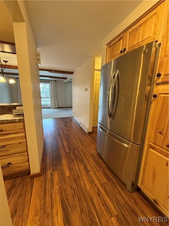 kitchen with brown cabinets, dark wood finished floors, freestanding refrigerator, dark stone counters, and baseboards