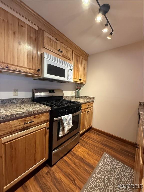 kitchen with dark wood finished floors, dark countertops, white microwave, stainless steel gas stove, and baseboards