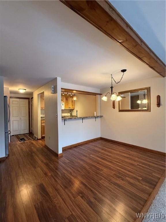 unfurnished living room featuring a chandelier, dark wood finished floors, beamed ceiling, and baseboards