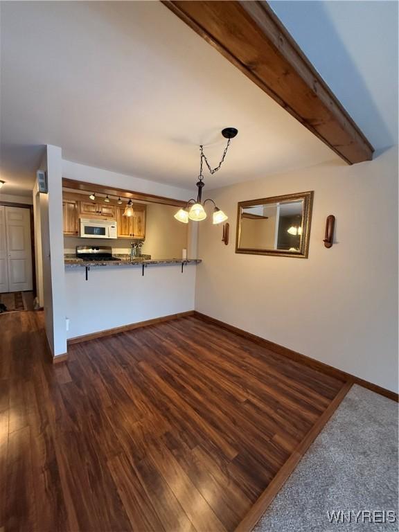 unfurnished living room featuring dark wood-type flooring, a chandelier, beamed ceiling, and baseboards