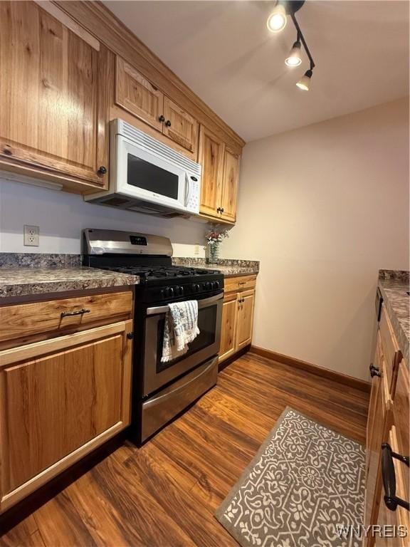 kitchen featuring dark wood finished floors, dark countertops, white microwave, brown cabinetry, and stainless steel gas stove