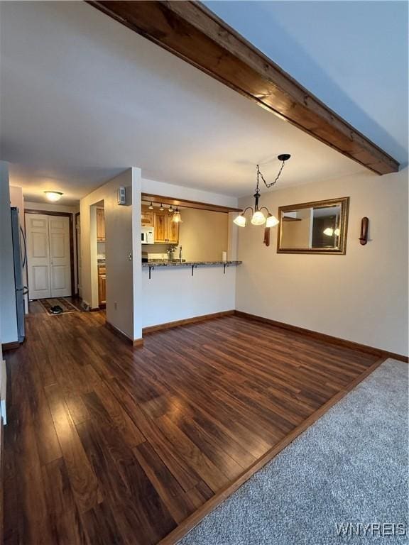 unfurnished living room featuring dark wood-style floors, beamed ceiling, an inviting chandelier, and baseboards