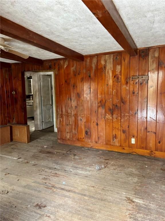 empty room with a textured ceiling, hardwood / wood-style floors, beamed ceiling, and wood walls