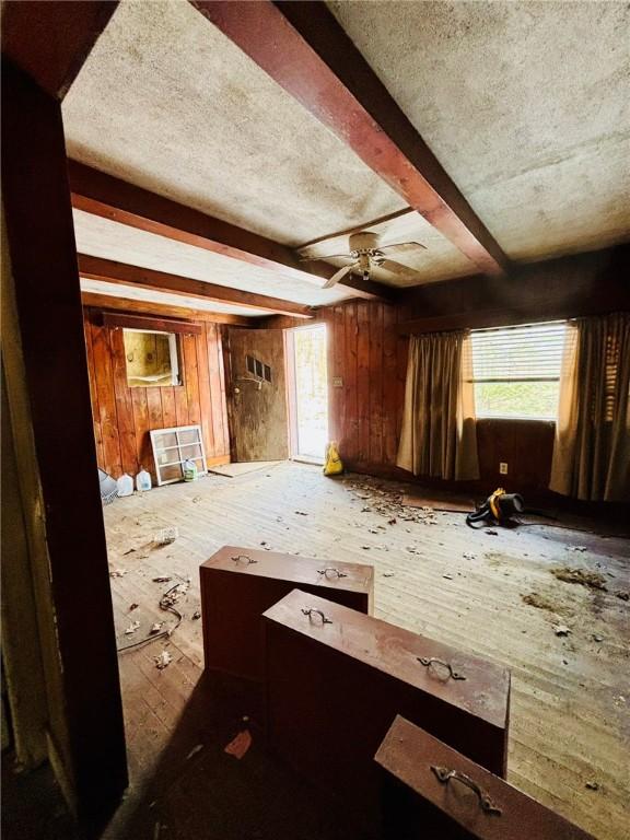 spare room featuring wood walls, ceiling fan, a textured ceiling, and beamed ceiling