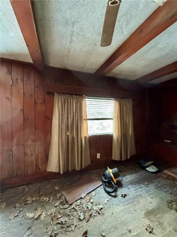 spare room with a textured ceiling, beam ceiling, and wooden walls