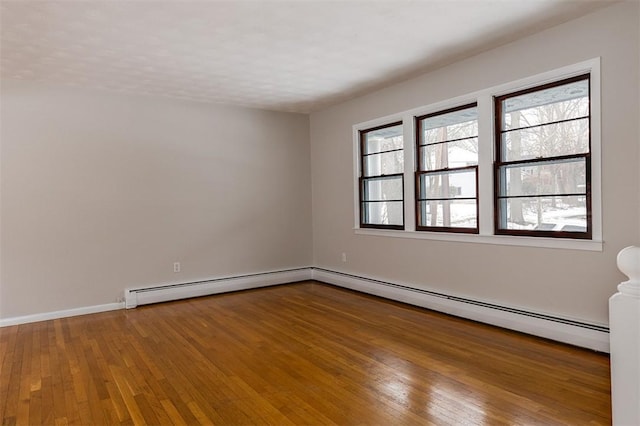 unfurnished room featuring baseboard heating, baseboards, and hardwood / wood-style floors