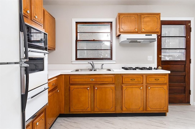 kitchen featuring under cabinet range hood, white appliances, a sink, light countertops, and brown cabinets