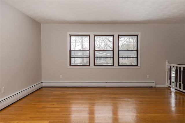 empty room featuring a baseboard radiator, plenty of natural light, a baseboard heating unit, and wood finished floors