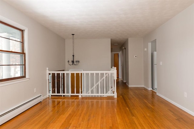 empty room featuring a baseboard heating unit, baseboards, a chandelier, and light wood-style floors