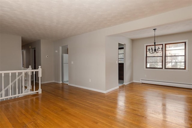 spare room featuring a baseboard radiator, baseboards, light wood finished floors, and an inviting chandelier