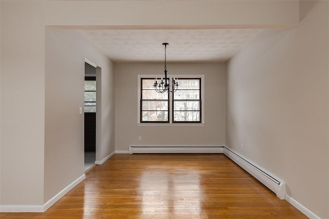 unfurnished dining area with a notable chandelier, a baseboard heating unit, wood finished floors, baseboards, and baseboard heating