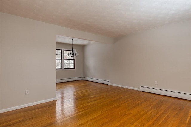 spare room with a chandelier, a baseboard heating unit, baseboards, baseboard heating, and light wood finished floors