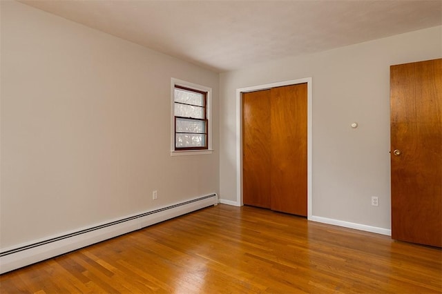 unfurnished bedroom featuring a closet, a baseboard radiator, wood finished floors, and baseboards