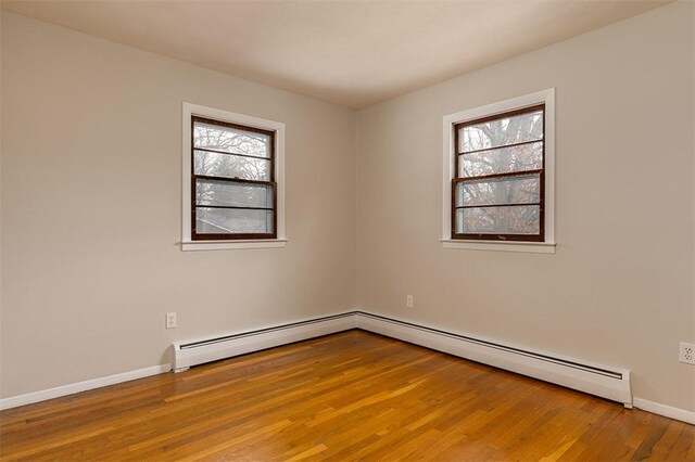 spare room with a baseboard radiator, plenty of natural light, baseboards, and wood finished floors