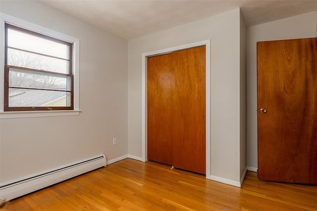 unfurnished bedroom with a baseboard heating unit, a closet, baseboards, and wood finished floors