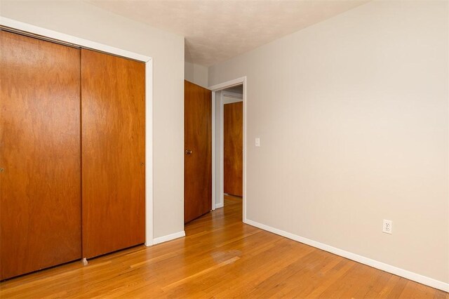 unfurnished bedroom featuring light wood finished floors, a closet, and baseboards