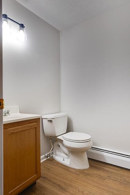 half bath featuring toilet, wood finished floors, baseboard heating, a textured ceiling, and vanity