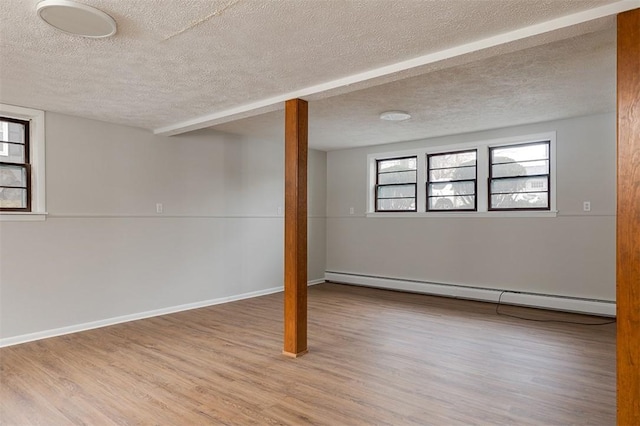 below grade area featuring baseboards, a textured ceiling, baseboard heating, and wood finished floors