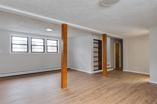 below grade area with a textured ceiling, a baseboard heating unit, baseboards, light wood-style floors, and stairway