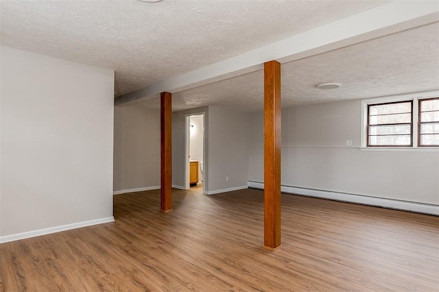 below grade area with light wood-type flooring, a textured ceiling, baseboards, and a baseboard radiator