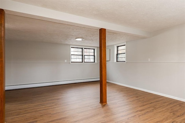 basement featuring a baseboard heating unit, a textured ceiling, baseboards, and wood finished floors