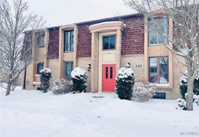 multi unit property with mansard roof, a shingled roof, and brick siding