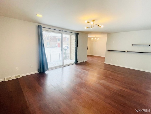 unfurnished room featuring baseboards, wood finished floors, visible vents, and a notable chandelier