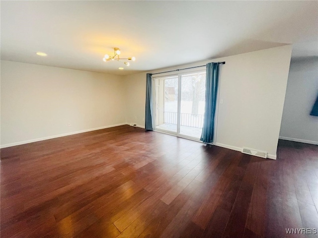 empty room featuring dark wood-type flooring, visible vents, a notable chandelier, and baseboards