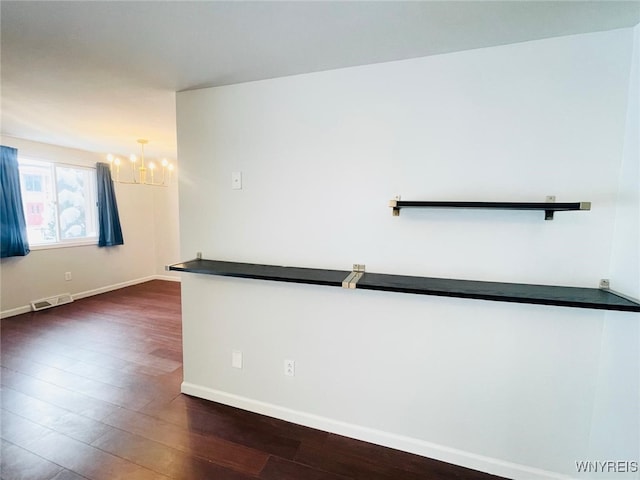 unfurnished room with an inviting chandelier, baseboards, visible vents, and dark wood finished floors