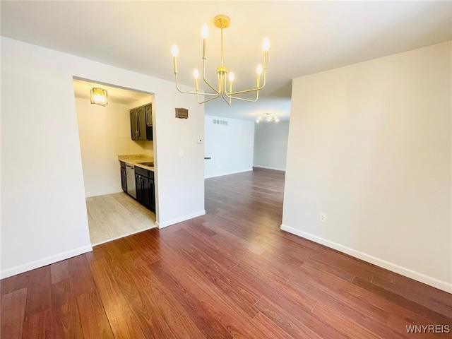 empty room with baseboards, visible vents, a chandelier, and wood finished floors